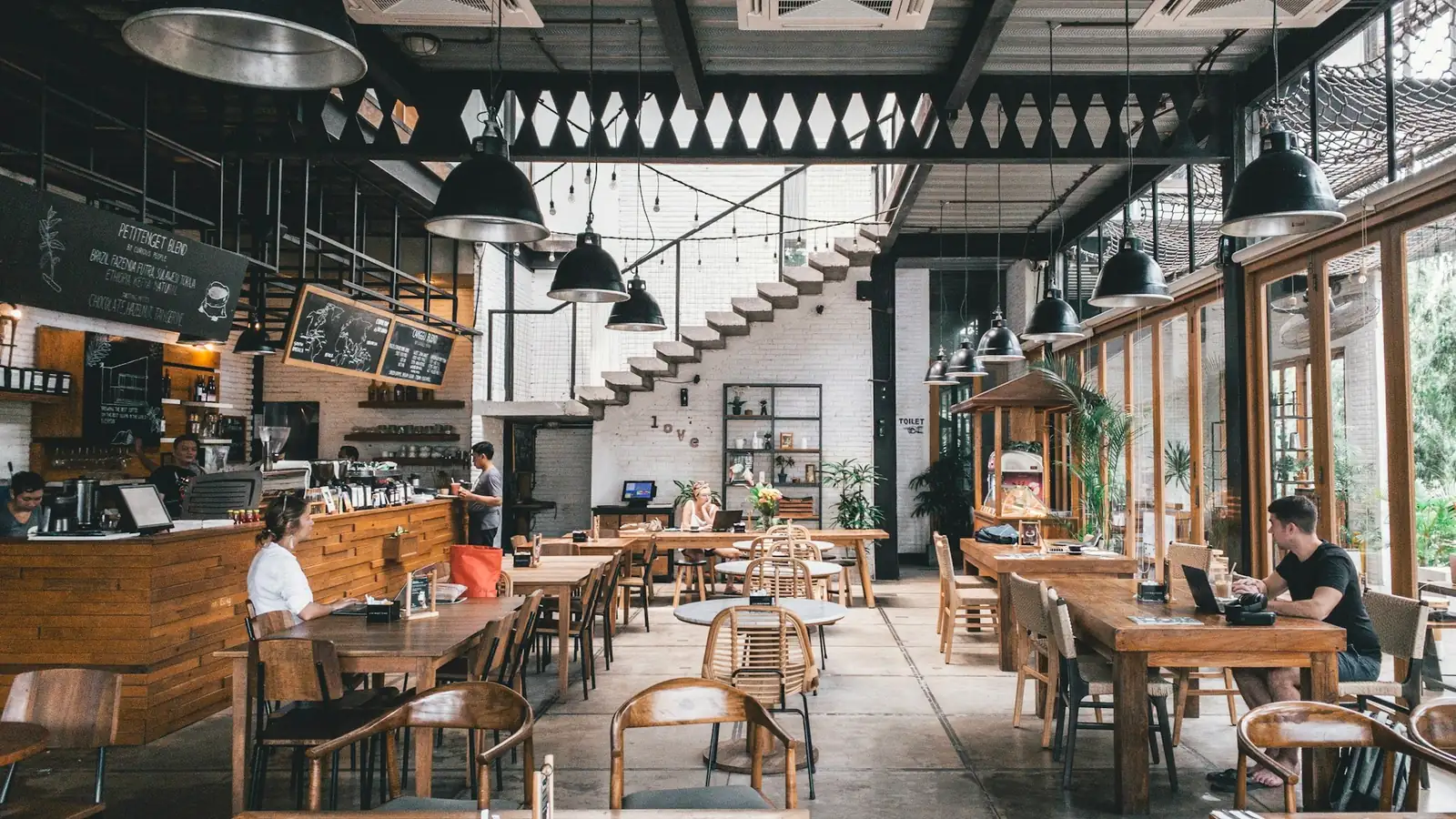 Ruim café met houten tafels, hanglampen en een bar met krijtborden